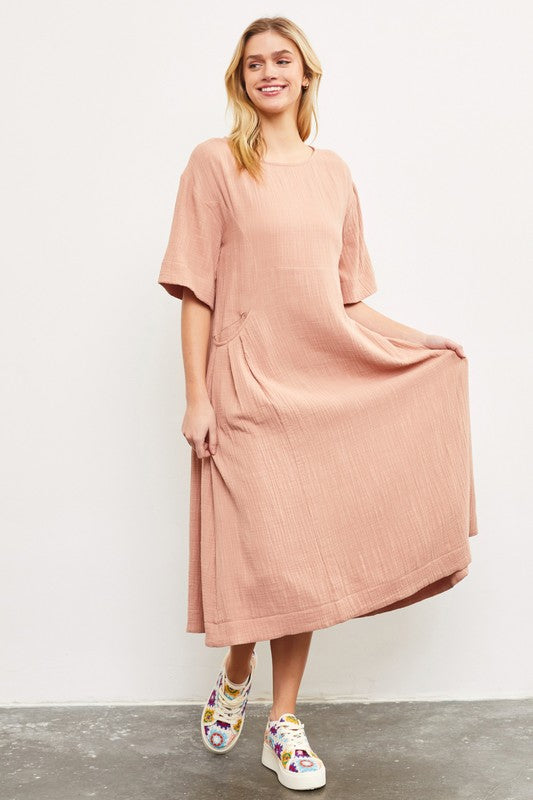 Woman wearing a blush pink cotton midi dress with side pockets.