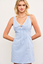 Model wearing blue checkered sleeveless mini dress with lace trim and tie front
