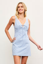 Model wearing blue checkered sleeveless mini dress with lace trim and tie front