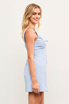 Model wearing blue checkered sleeveless mini dress with lace trim and tie front
